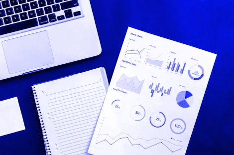 A desk with a laptop, notebook, and a printed sheet showing charts and graphs
