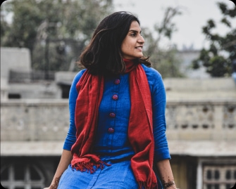 Young woman smiling while sitting outside in a blue dress and red scarf