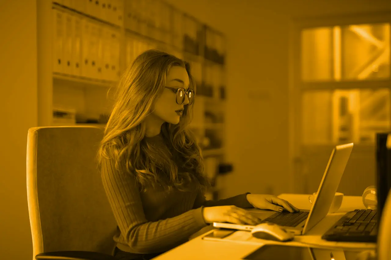 Remote worker with long hair and glasses working on a laptop at an office desk